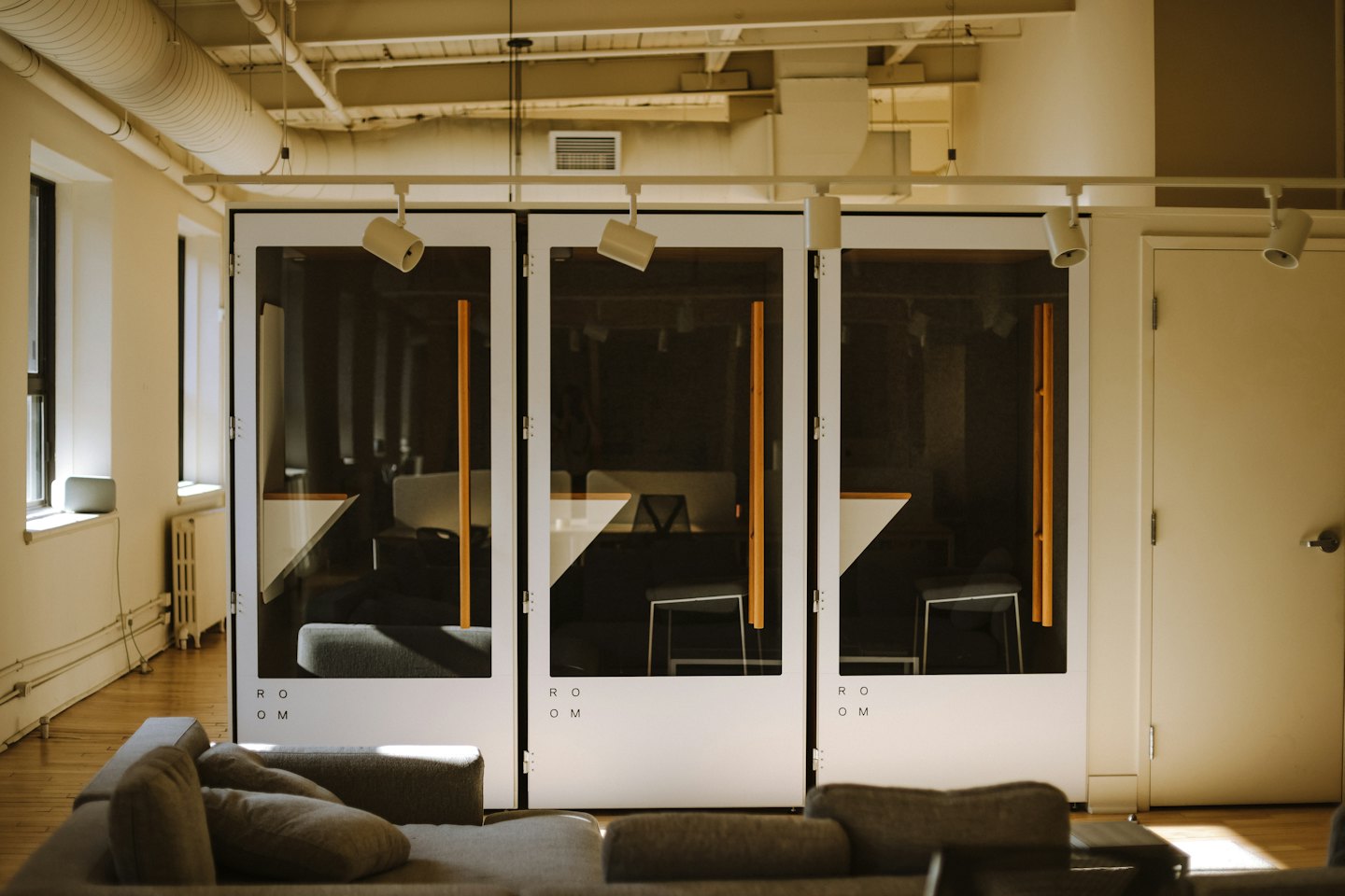 Oficina moderna con sofá modular y salas de reuniones acristaladas.