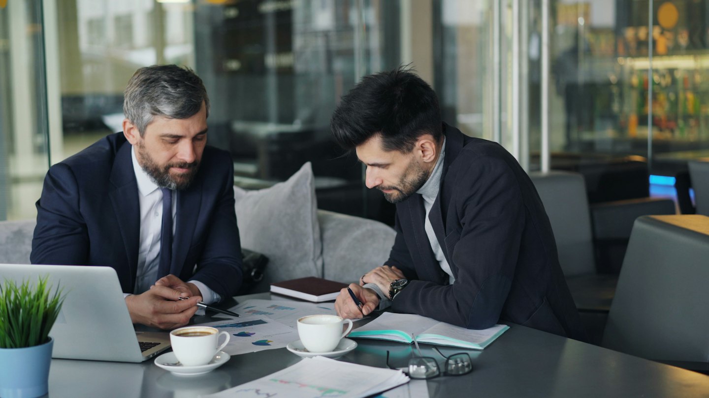 Dos hombres de negocios analizan gráficos financieros en una mesa.